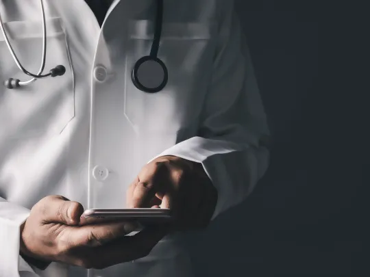 طبيب يُطّلع على هاتفه لمعرفة المزايا المتعلقة بباقة الأطباء من بنك بوبيان.